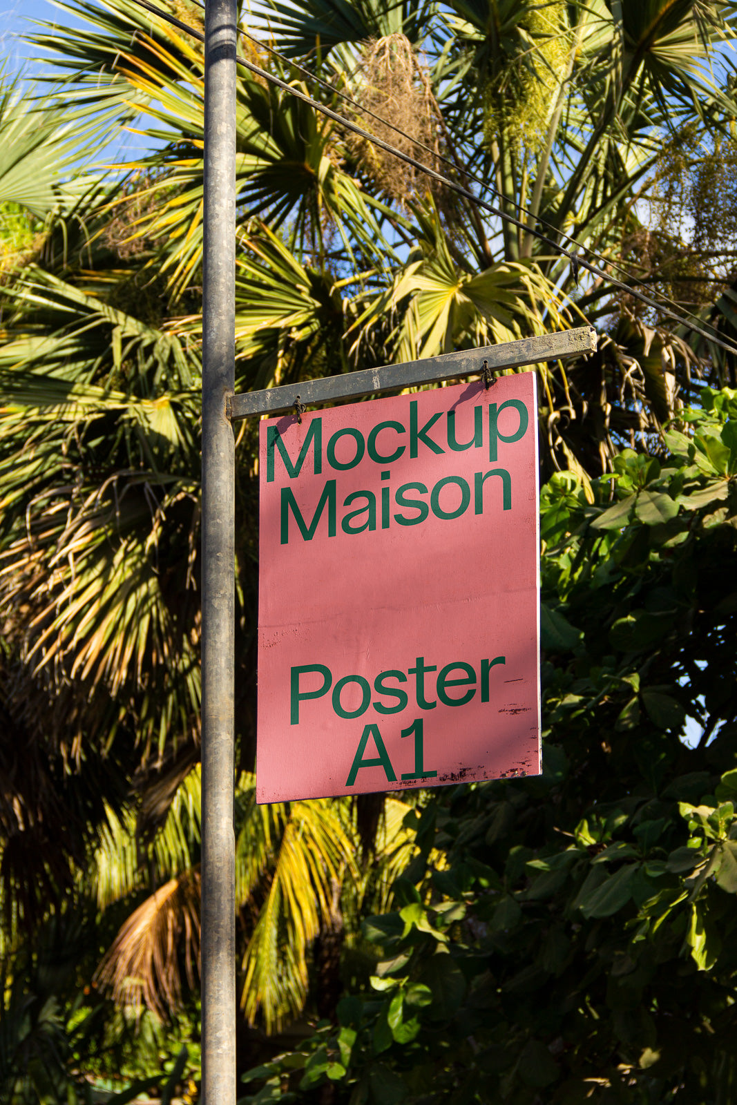 PSD mockup of a pink poster labeled "Mockup Maison Poster A1," hanging on a metal pole with a background of lush palm trees.