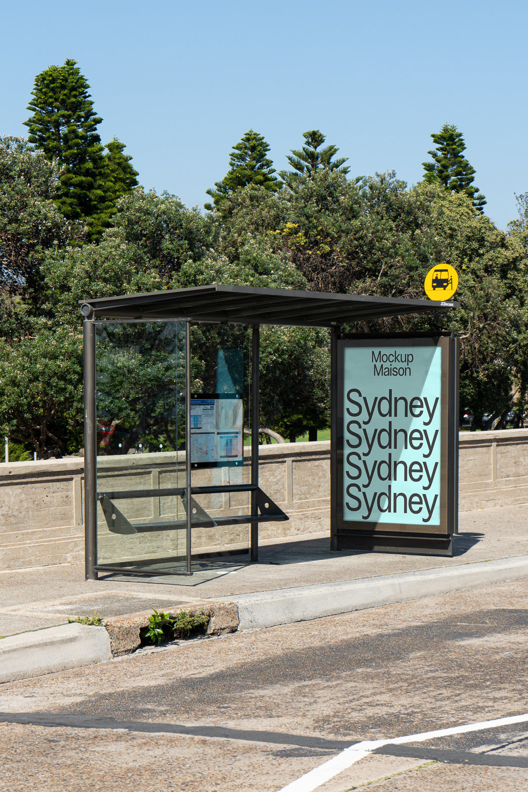 PSD mockup of a modern bus stop shelter with a large advertisement displaying repeated text "Sydney" against a clear sky and trees in the background.