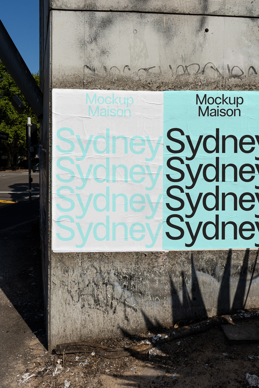 PSD mockup of posters on a concrete wall displaying "Sydney" in pastel blue and black text, with shadows cast by nearby trees.
