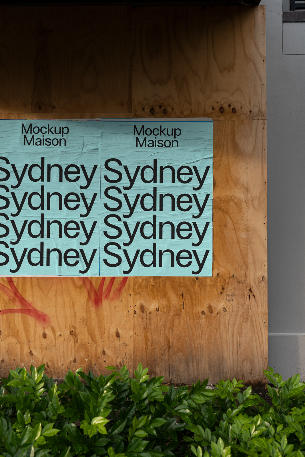 PSD mockup of posters on a wooden wall displays the repeated word "Sydney" in bold black letters on a light blue background with greenery at the bottom.