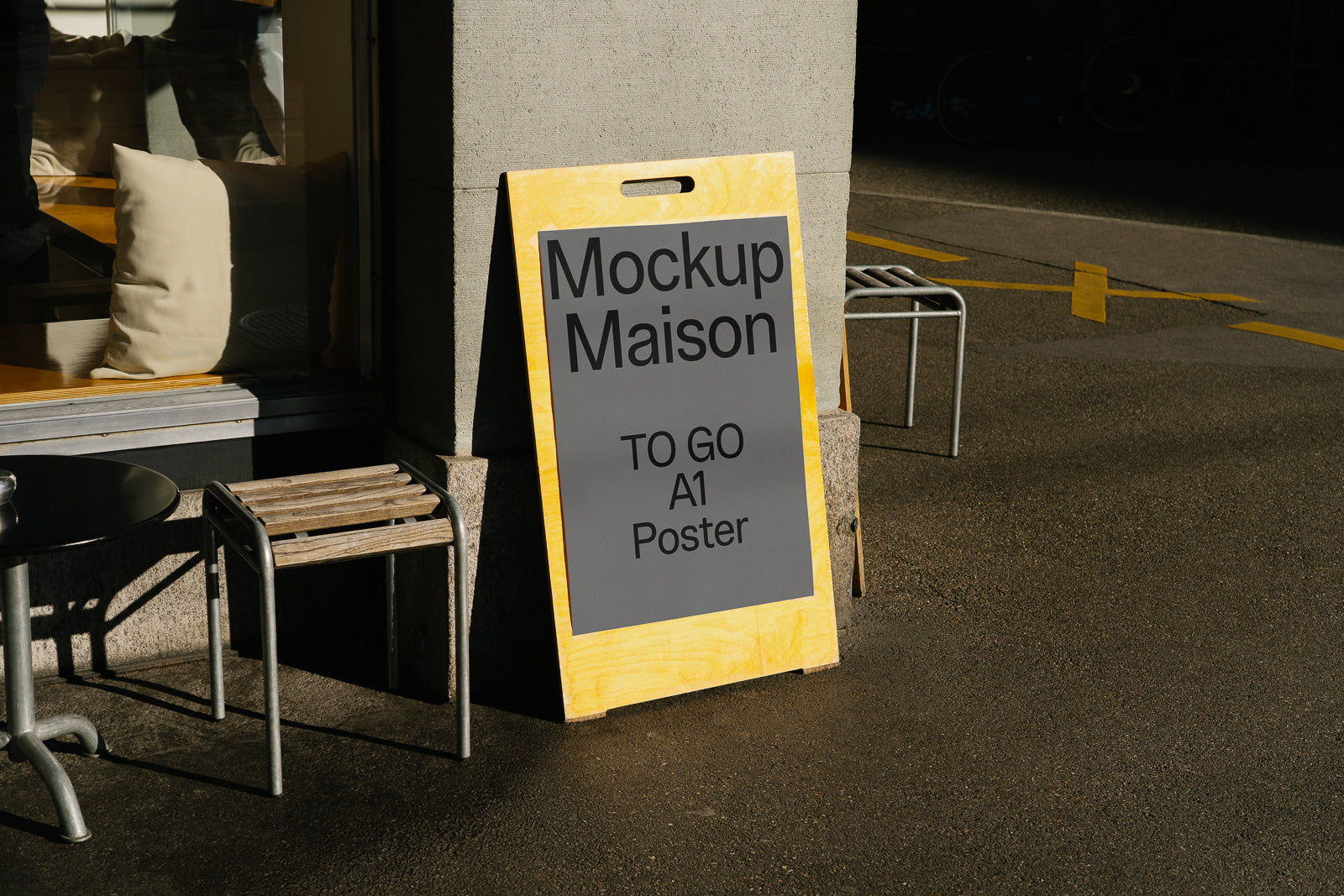 PSD mockup of a vertical yellow sandwich board with "Mockup Maison TO GO A1 Poster" text, outside a building with seating visible nearby.