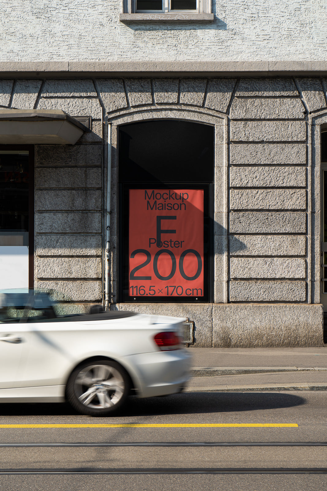 PSD mockup of a large poster displayed in a street-facing window on a stone building with a passing white convertible in the foreground.