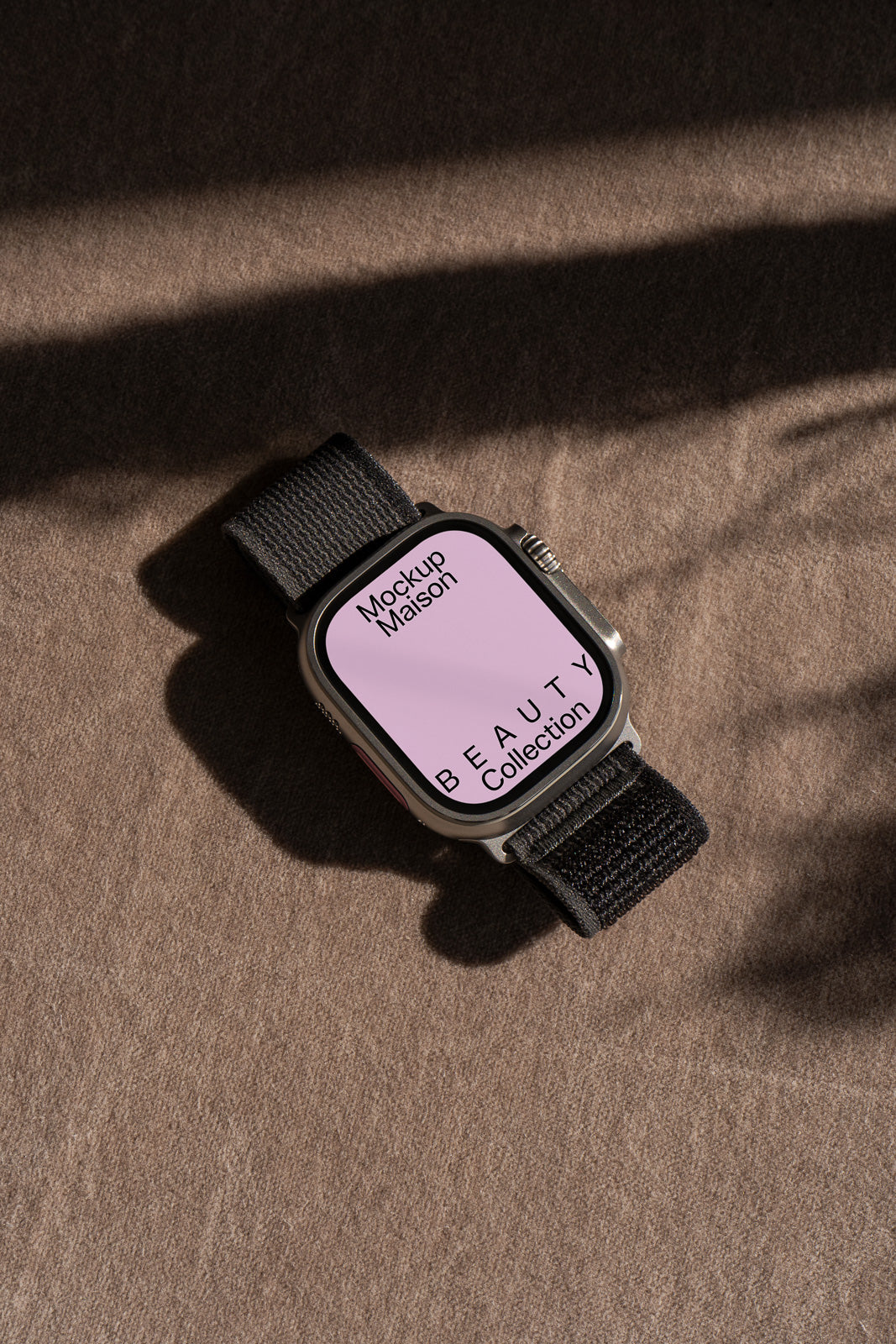 PSD mockup of a smartwatch with a black band and a pink screen displaying text, placed on a textured brown surface with shadows.