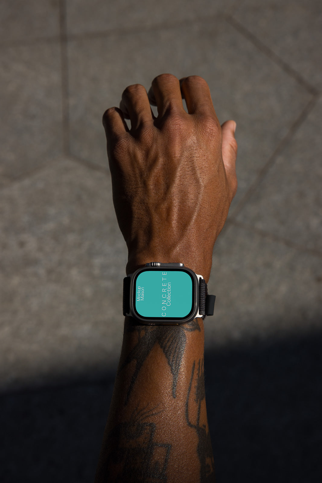 PSD mockup of a smartwatch with a dark face and strap on a wrist. The watch screen displays text vertically on a turquoise background, with focus on concrete texture.