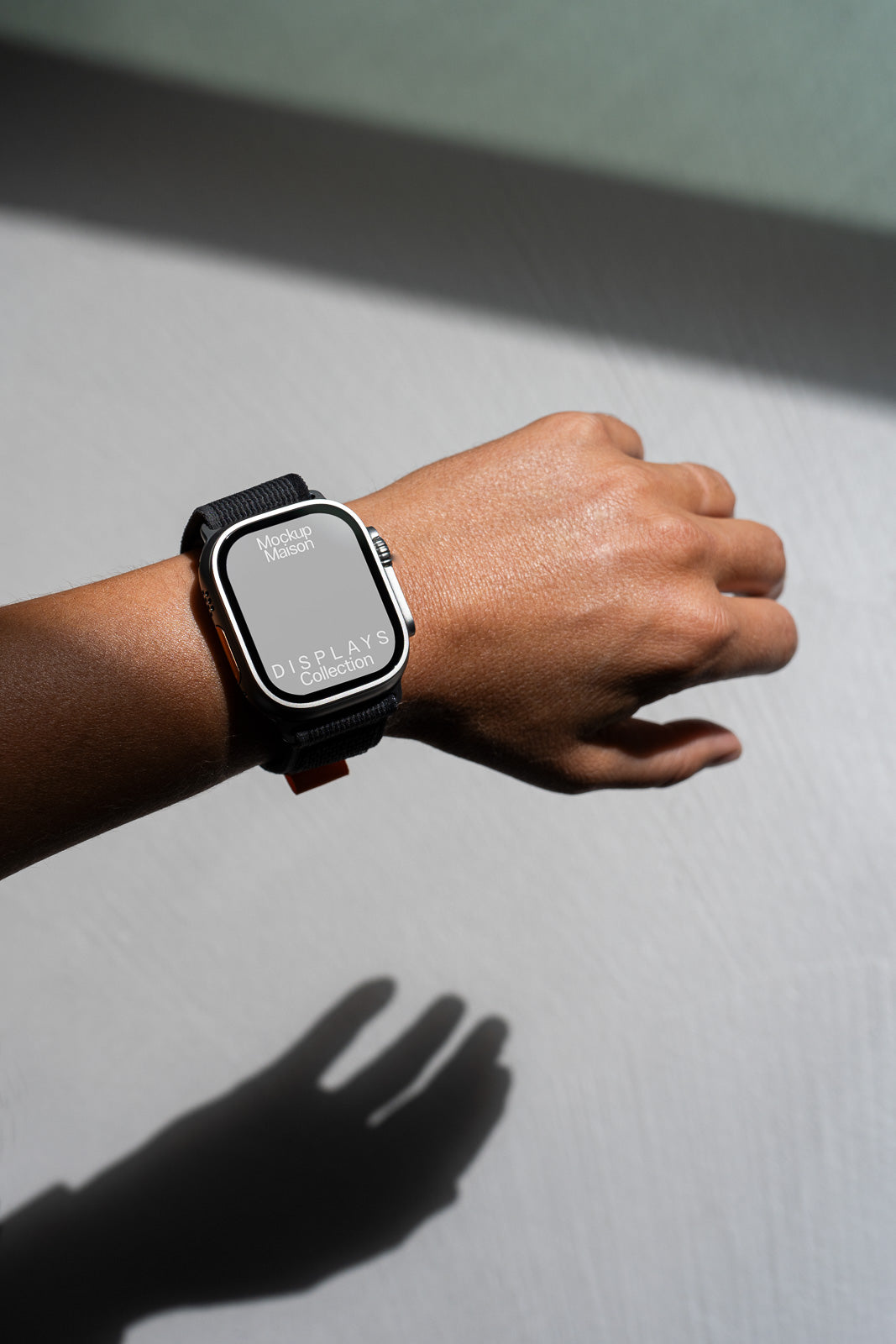 PSD mockup of a smartwatch with a black band on a person's wrist, casting a shadow on a light gray surface.