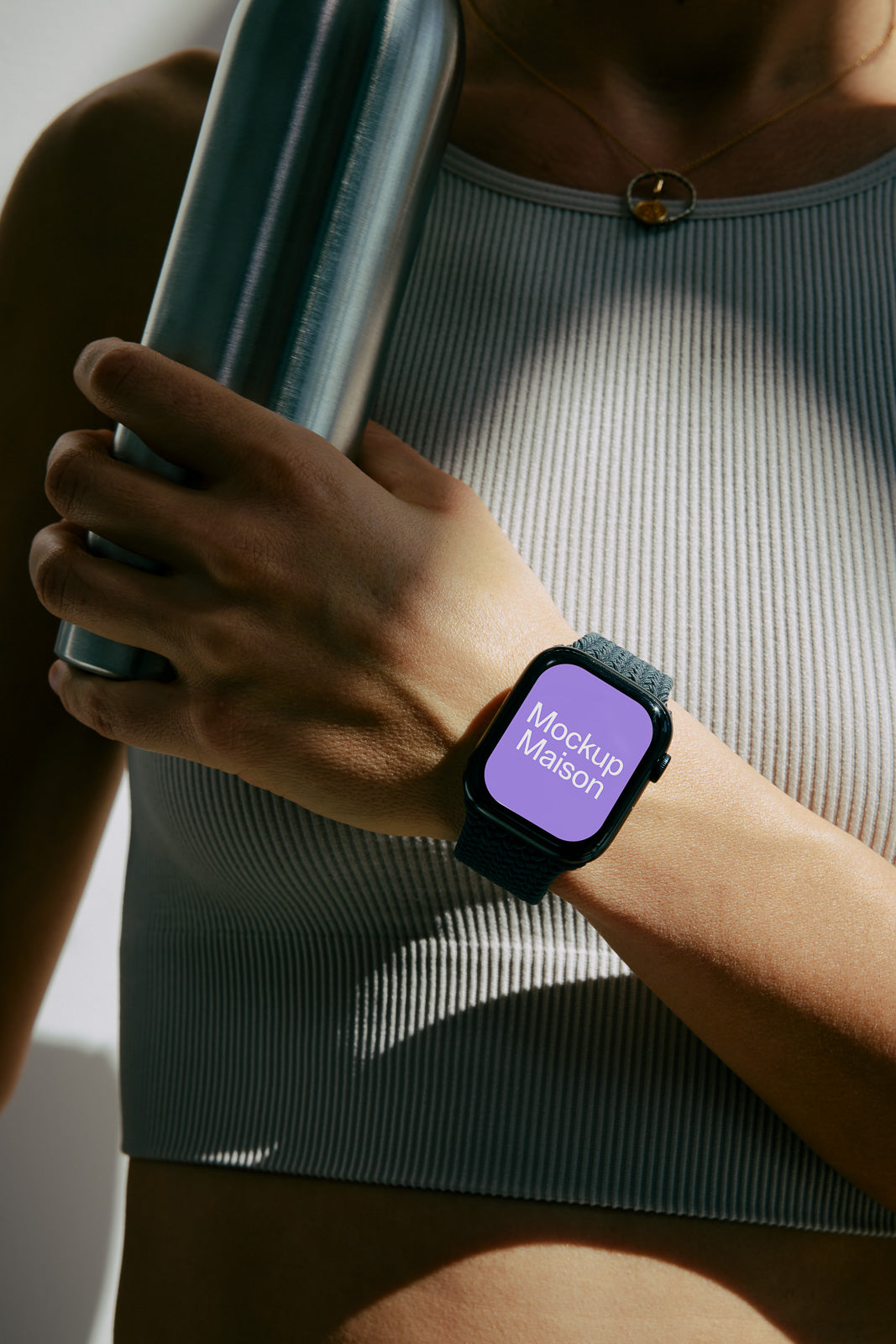 PSD mockup of a smartwatch on a person's wrist, displaying "Mockup Maison," while the person holds a metallic water bottle.