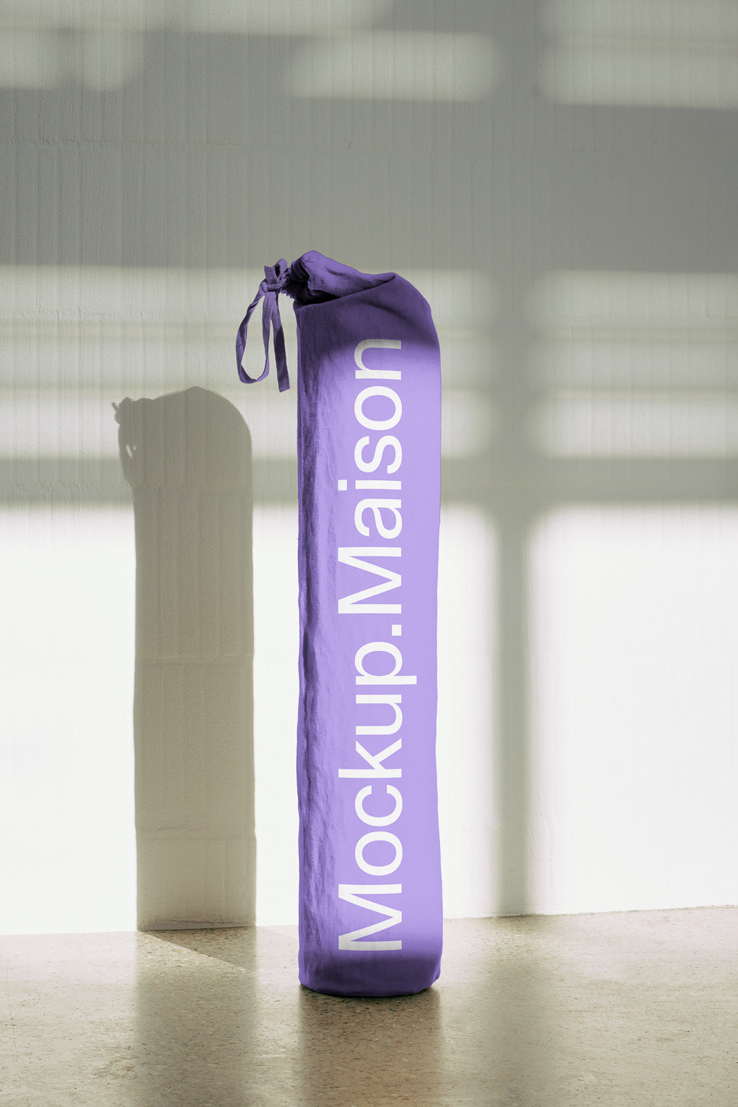 PSD mockup of a purple fabric bag with "Mockup.Maison" text, standing upright on a textured floor with a soft shadow on a light wall.