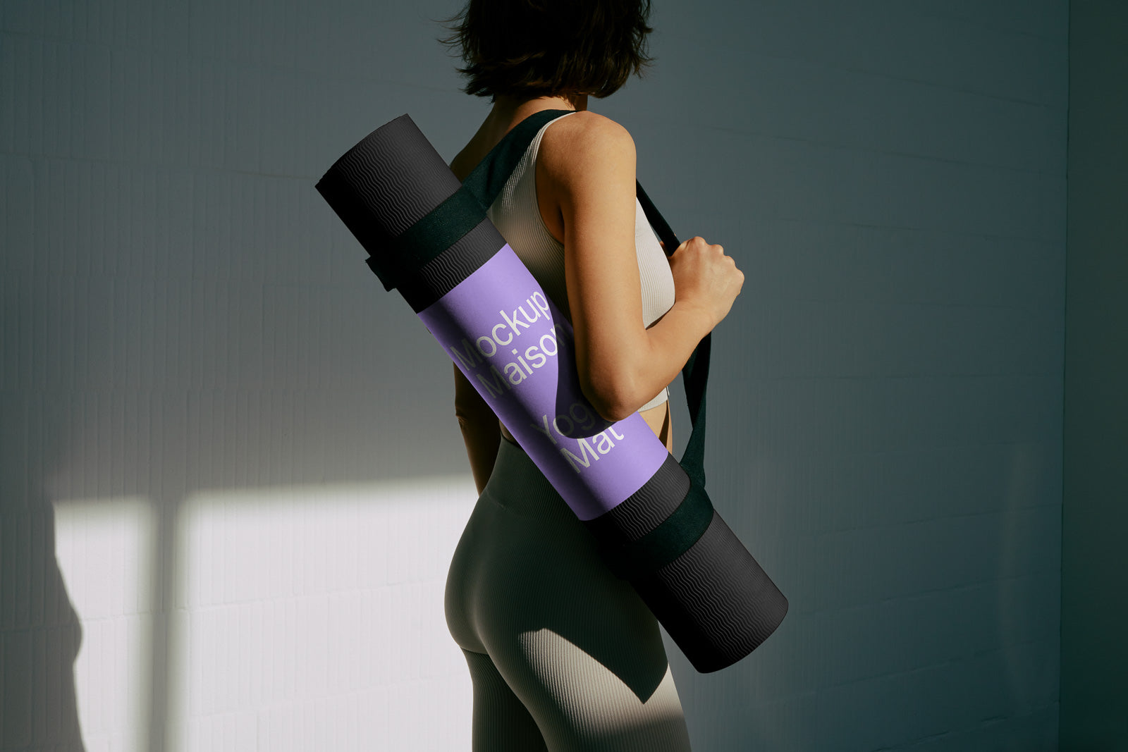 PSD mockup of a person carrying a rolled-up yoga mat in a strap over their shoulder, wearing a light-colored athletic outfit against a dark background.