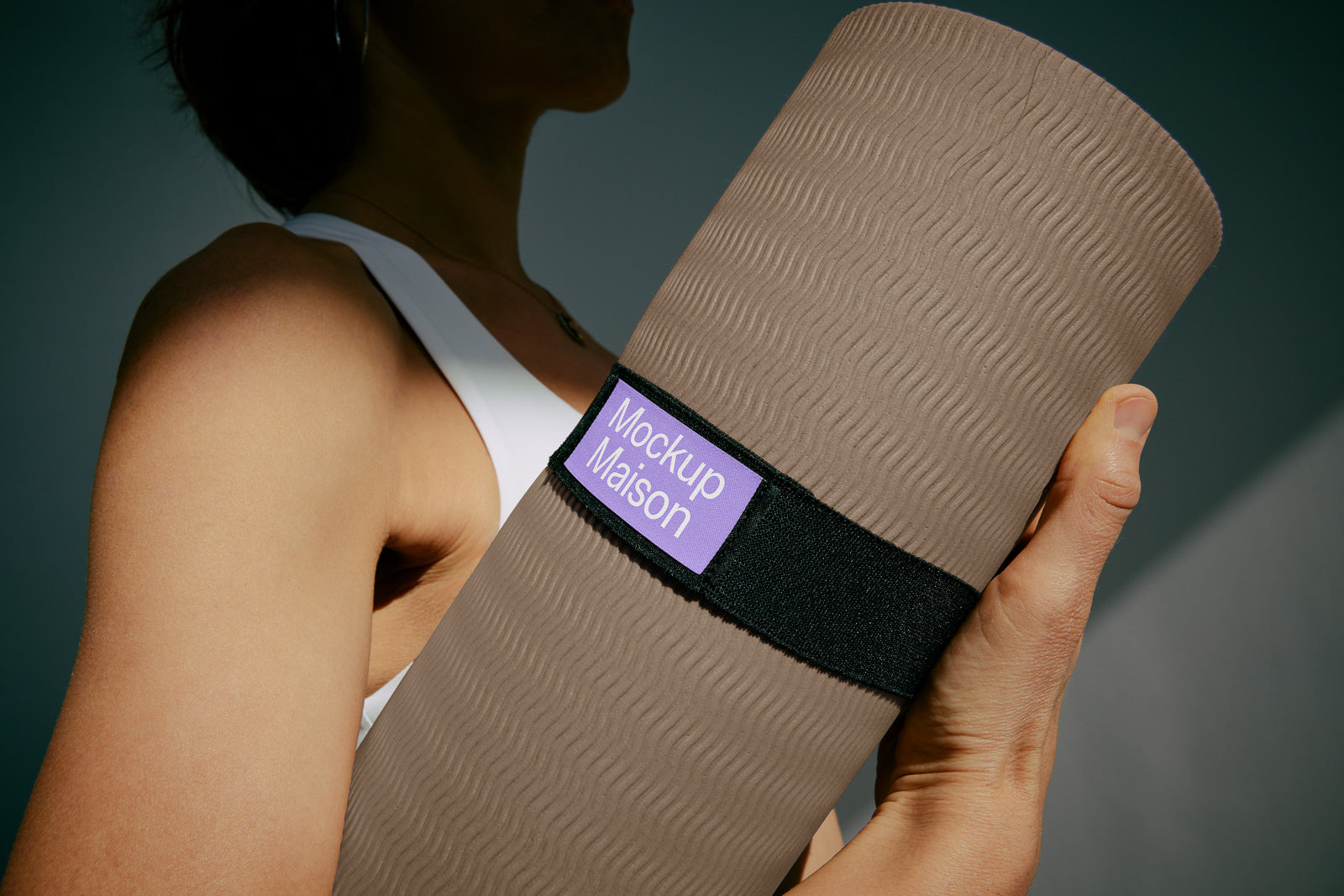 PSD mockup of a person holding a rolled yoga mat with textured surface and a label reading "Mockup Maison," showcasing the detail and grip.