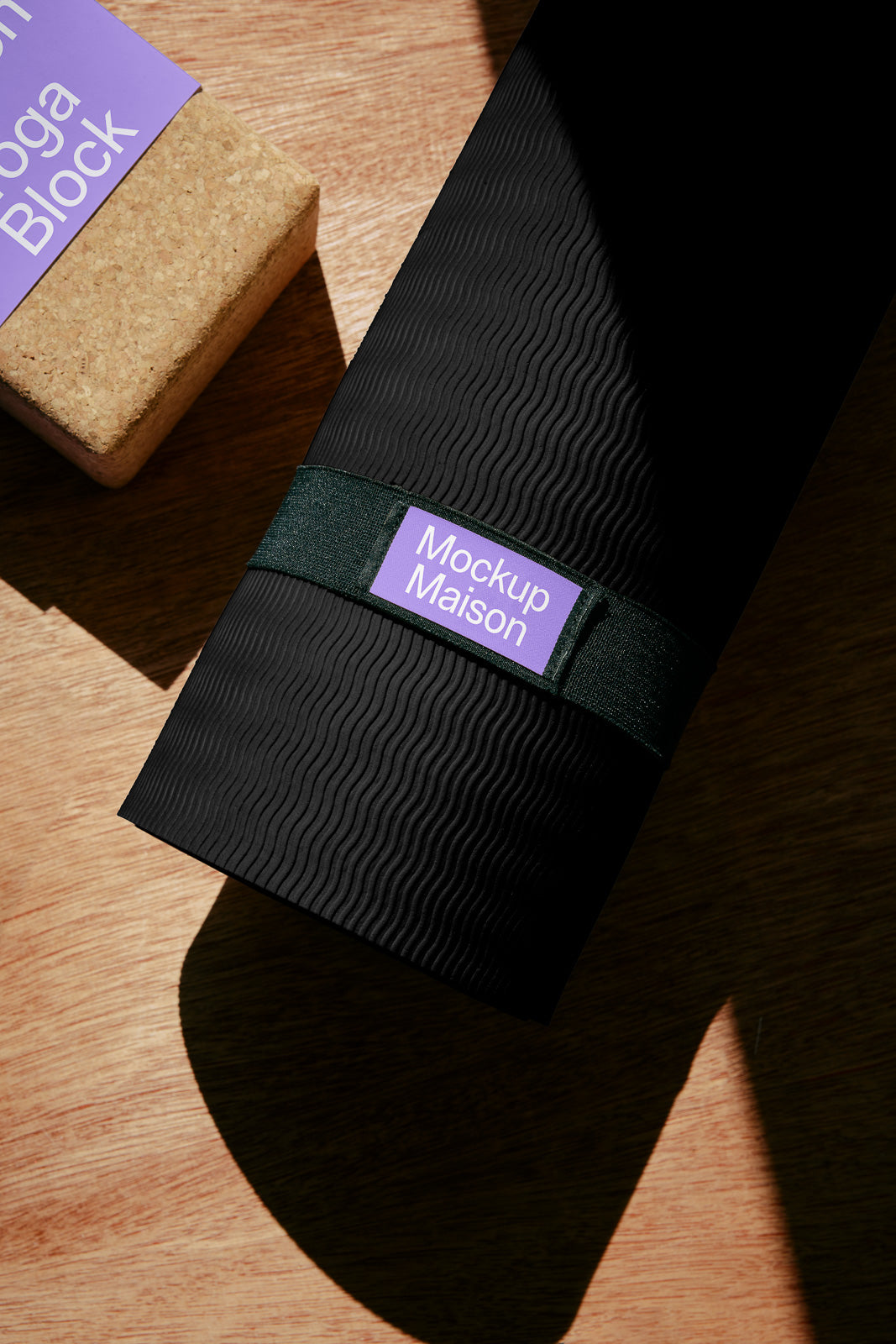 PSD mockup of a cork yoga block and rolled-up black yoga mat with labels on a wooden surface, showcasing branding elements.