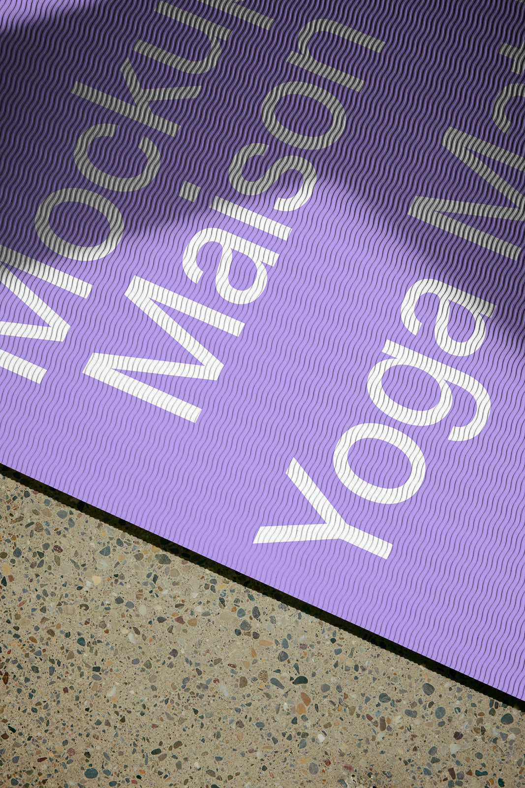 PSD mockup of a purple yoga mat with white text featuring a wavy pattern on a speckled floor.